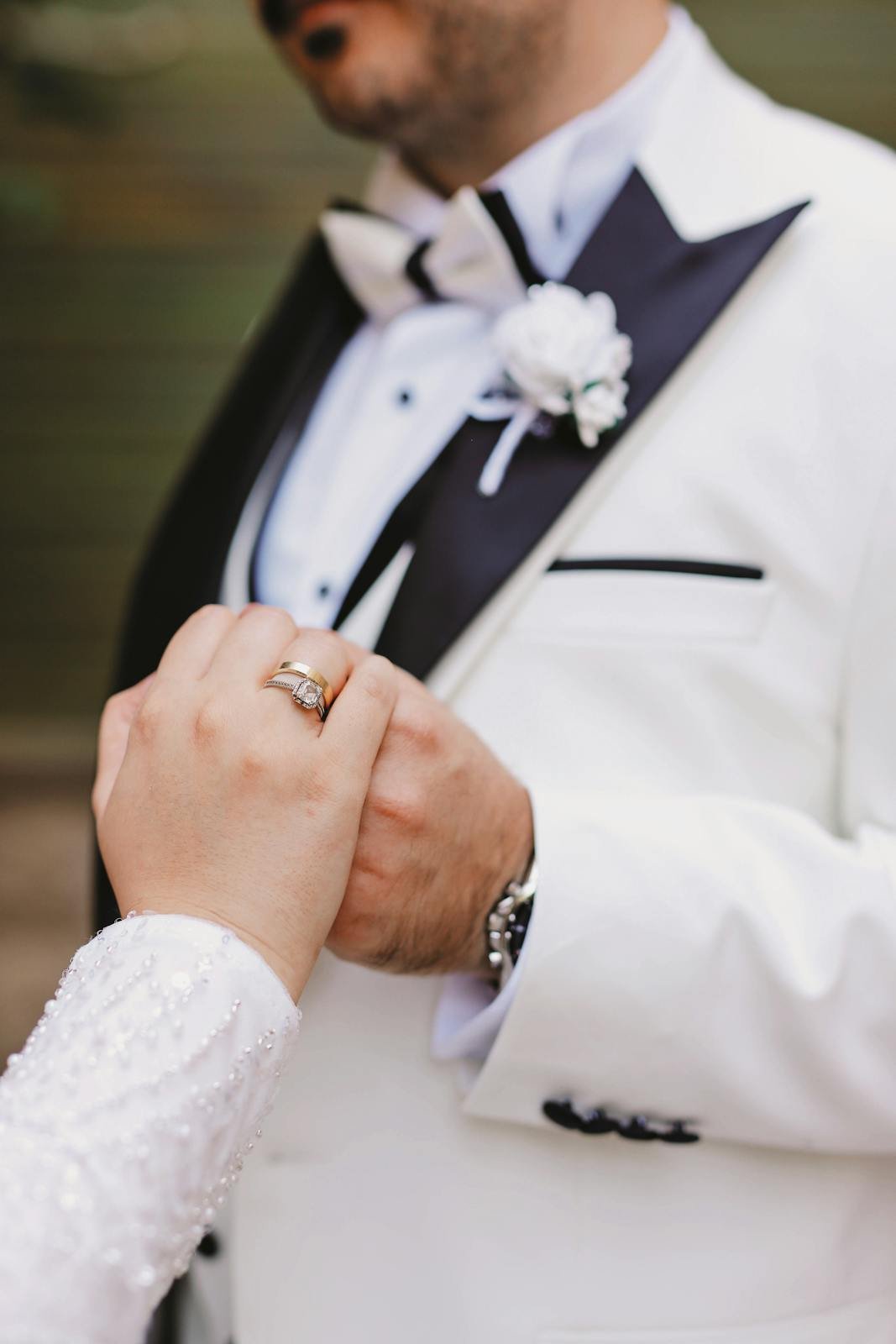 Close-up of a groom in a tuxedo holding hands with a bride, symbolizing love and commitment.